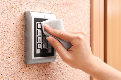 Woman using tissue paper to press keys of digital access lock, closeup