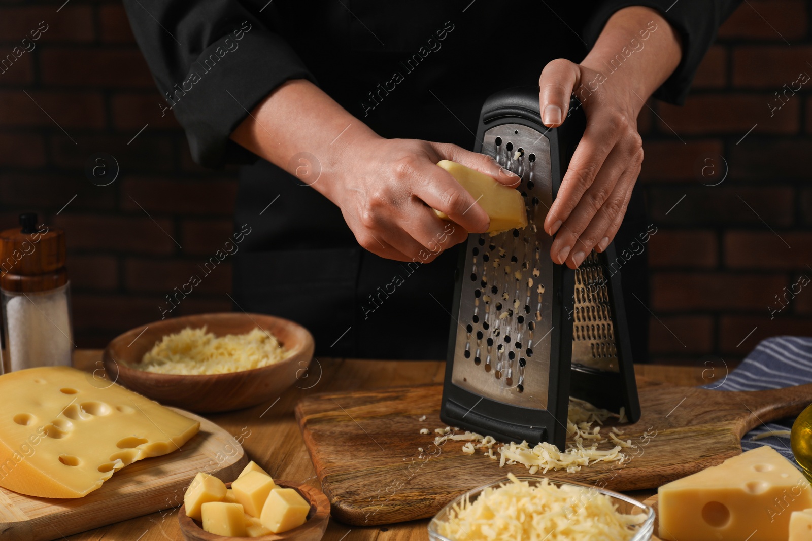 Photo of Woman grating cheese at wooden table, closeup