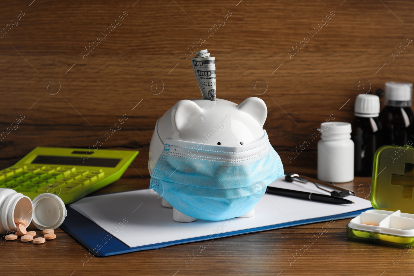 Photo of White ceramic piggy bank with mask, money and pills on wooden table. Medical insurance