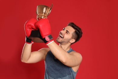 Photo of Portrait of happy young boxer with gold trophy cup on red background