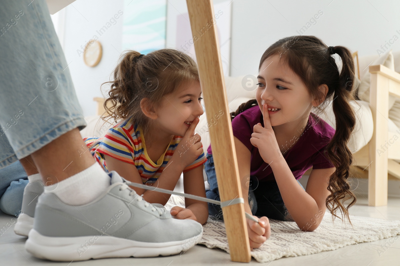 Photo of Cute little children tying shoe laces of their father together at home, closeup