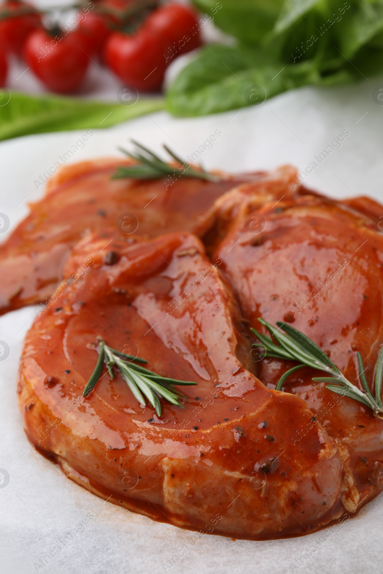 Photo of Raw marinated meat and rosemary on parchment, closeup