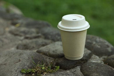 Photo of Cardboard takeaway coffee cup with lid on stones outdoors, space for text