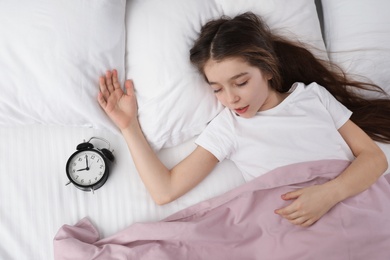 Beautiful little girl with alarm clock sleeping in bed, top view