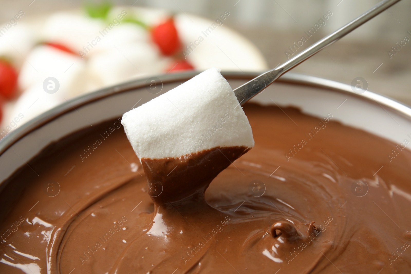 Photo of Dipping marshmallow into pot with tasty chocolate fondue, closeup