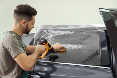 Worker tinting car window with heat gun in workshop