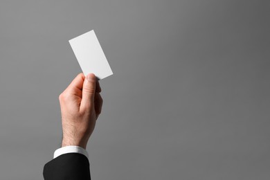 Photo of Man holding blank business card on grey background, closeup. Space for text