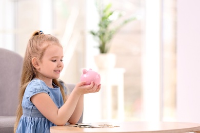 Little girl with piggy bank and money at home. Space for text