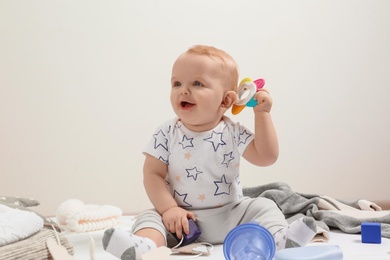 Little boy in cute clothes sitting on floor against light background. Baby accessories