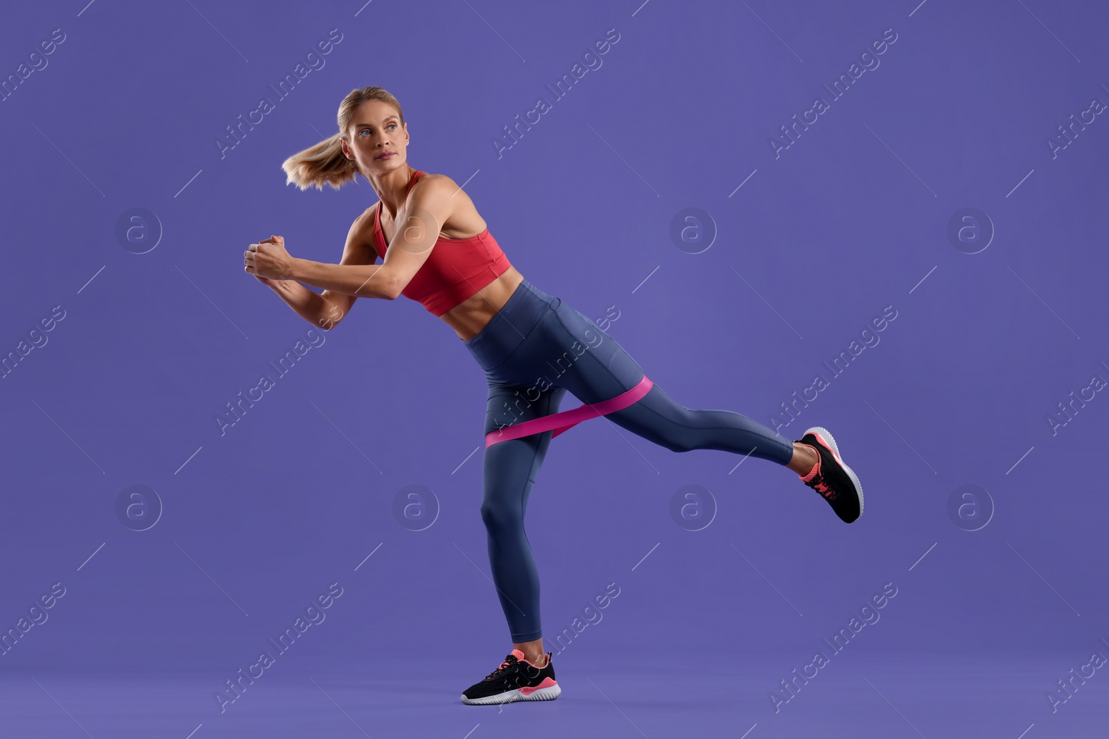 Photo of Athletic woman exercising with elastic resistance band on purple background