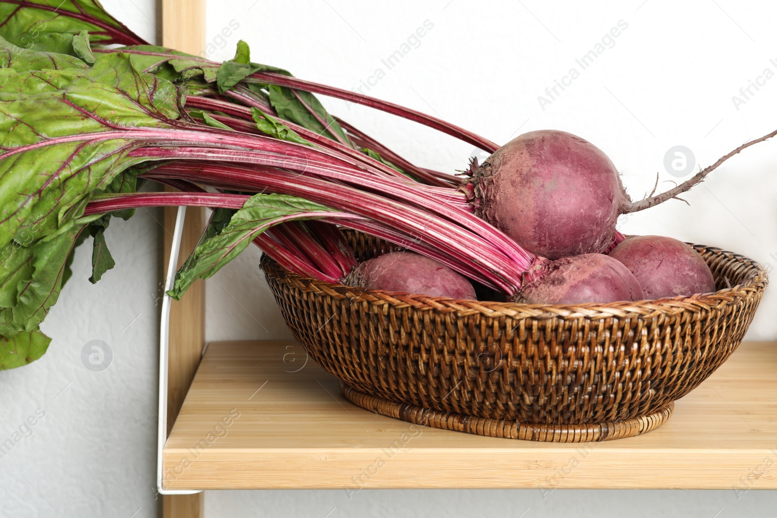 Photo of Raw ripe beets in wicker bowl on shelf indoors