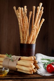 Photo of Delicious grissini sticks, oil, rosemary and tomatoes on wooden table