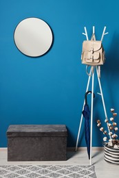 Photo of Stylish hallway with blue wall, mirror and clothing rack. Interior design