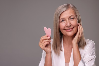 Woman with rose quartz gua sha tool on grey background, space for text. Facial massage