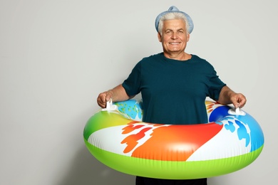 Funny mature man with bright inflatable ring on light background, space for text