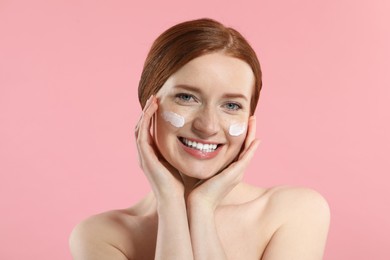 Photo of Smiling woman with freckles and cream on her face against pink background