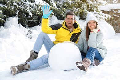 Happy couple with ball for snowman outdoors. Winter vacation