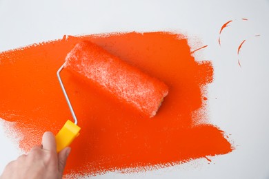 Photo of Man applying orange paint with roller brush on white background, closeup