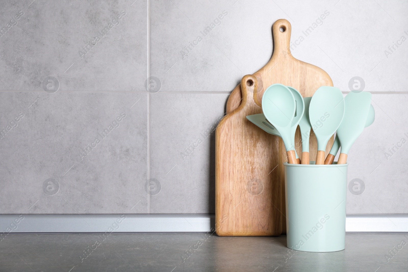 Photo of Holder with kitchen utensils and cutting boards on grey table. Space for text