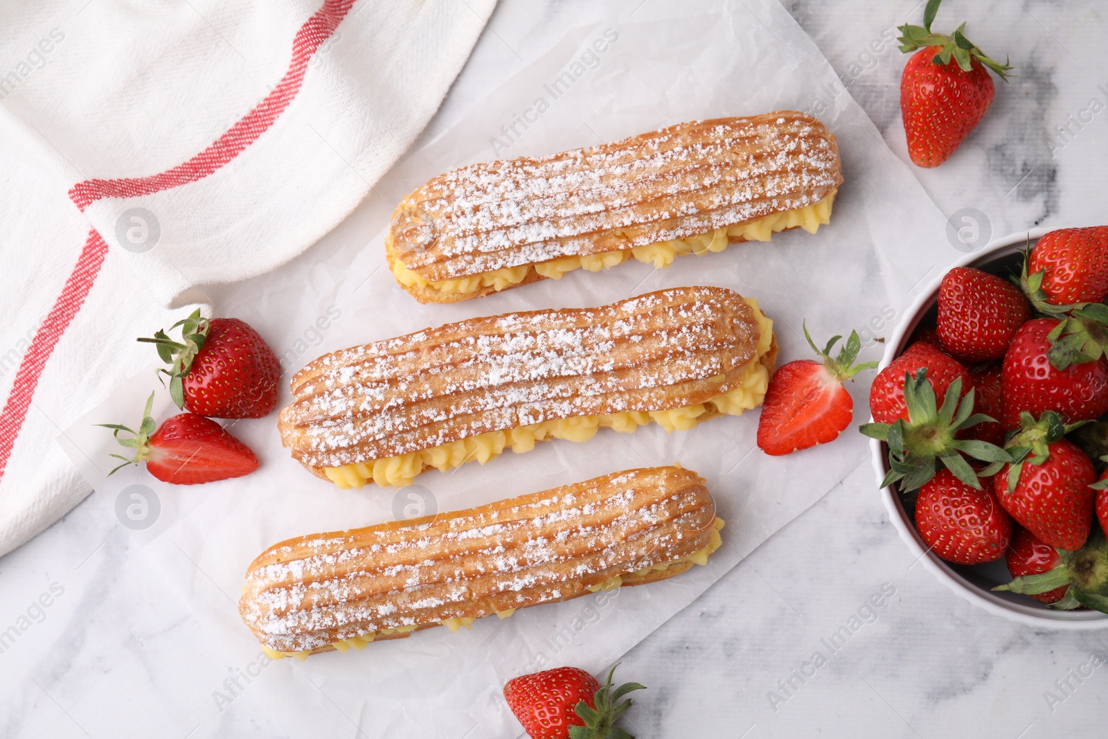 Photo of Delicious eclairs filled with cream and strawberries on white marble table, top view