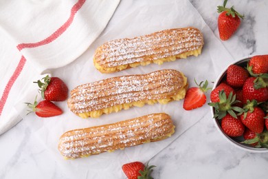 Photo of Delicious eclairs filled with cream and strawberries on white marble table, top view