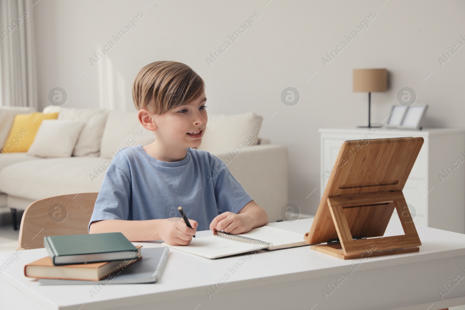 Photo of Boy doing homework with tablet at table indoors