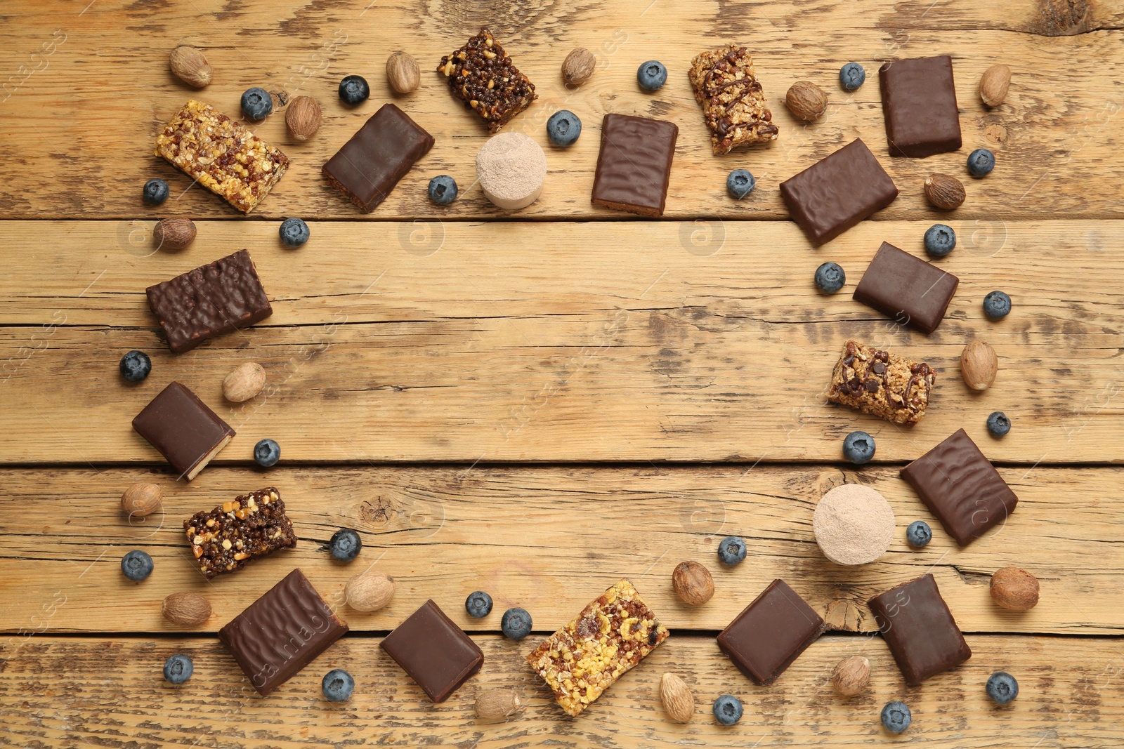 Photo of Frame of different energy bars, nuts, blueberries and protein powder on wooden table, flat lay. Space for text