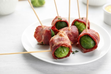 Photo of Plate with Brussels sprouts wrapped in bacon on white table, closeup