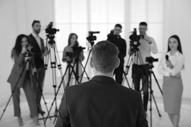 Businessman giving interview to journalists indoors, back view. Black and white effect