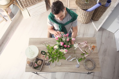 Male decorator creating beautiful bouquet at table, top view