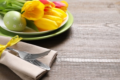 Photo of Festive Easter table setting with painted egg and flowers on wooden background, closeup. Space for text