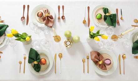 Photo of Festive Easter table setting with painted eggs, burning candles and yellow tulips, flat lay