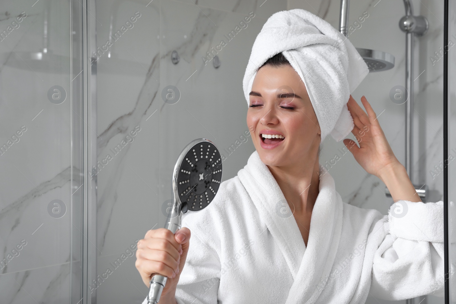 Photo of Beautiful young woman singing into showerhead in bathroom