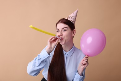 Photo of Young woman in party hat with blower and balloon on beige background