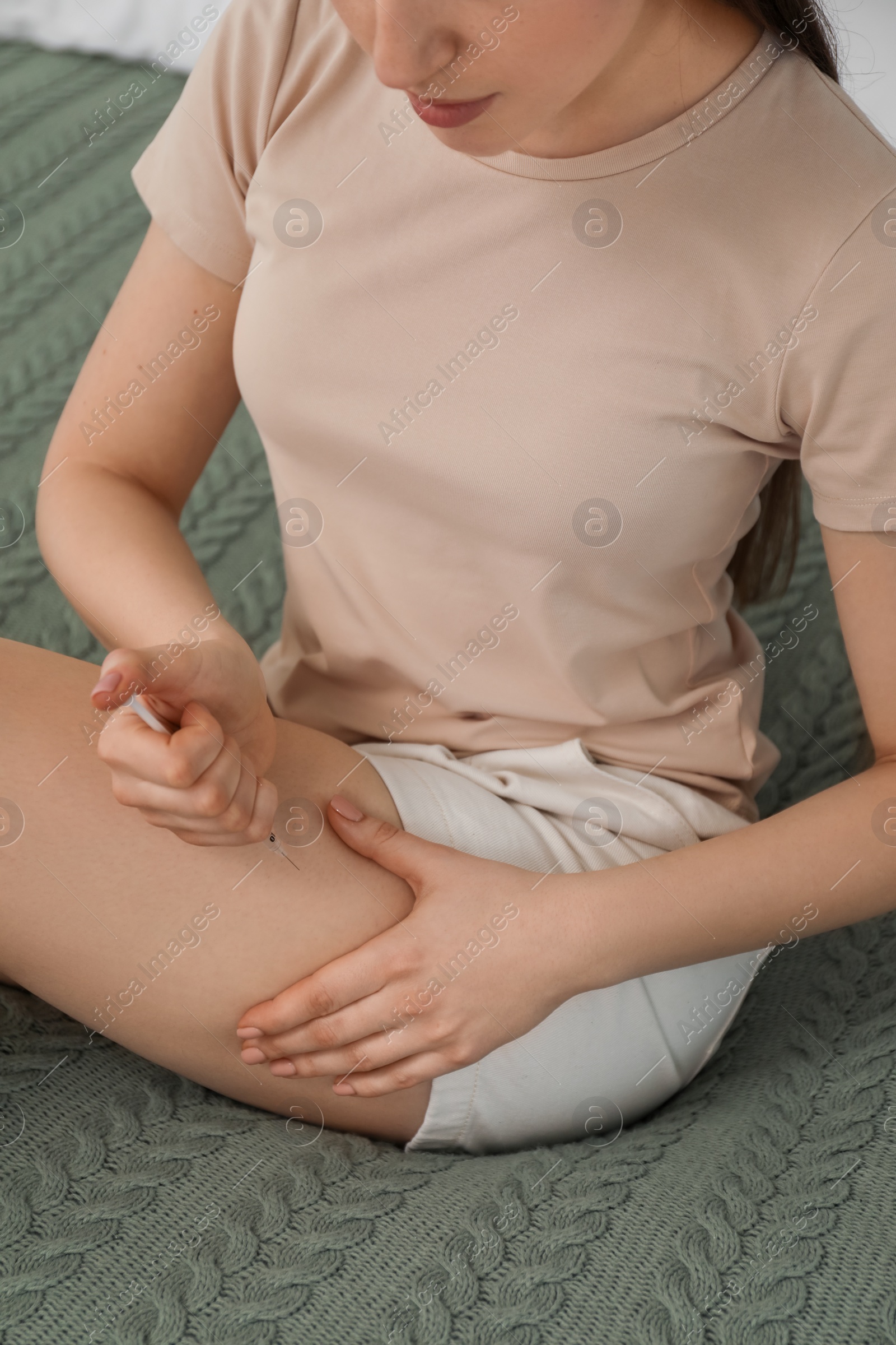 Photo of Diabetes. Woman making insulin injection into her leg on bed indoors, closeup