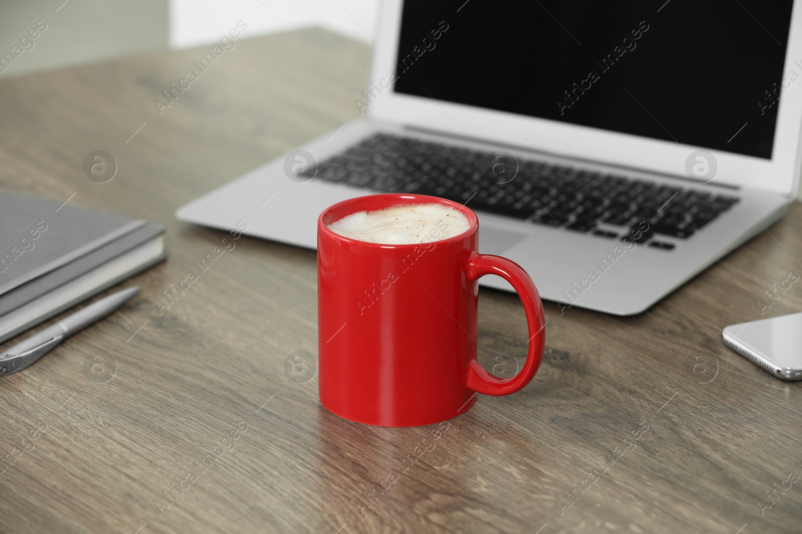 Photo of Red ceramic mug with hot drink on wooden table desk at workplace. Mockup for design