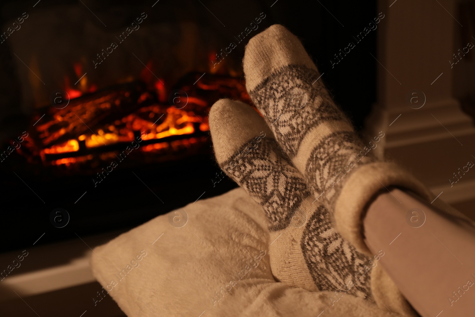 Photo of Woman in warm socks resting near fireplace with burning woods indoors, closeup