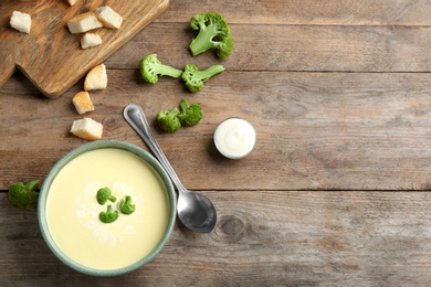 Flat lay composition with bowl of cheese cream soup and broccoli on wooden table, space for text