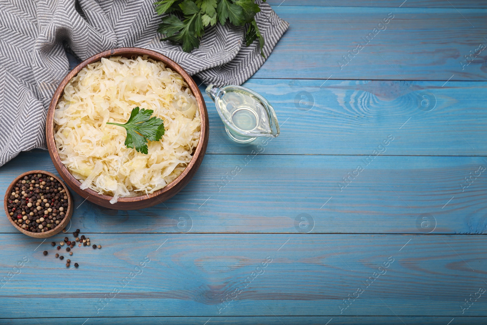 Photo of Bowl of tasty sauerkraut and ingredients on light blue wooden table, flat lay. Space for text