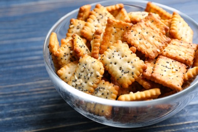 Photo of Delicious crispy crackers in bowl on blue wooden table, closeup