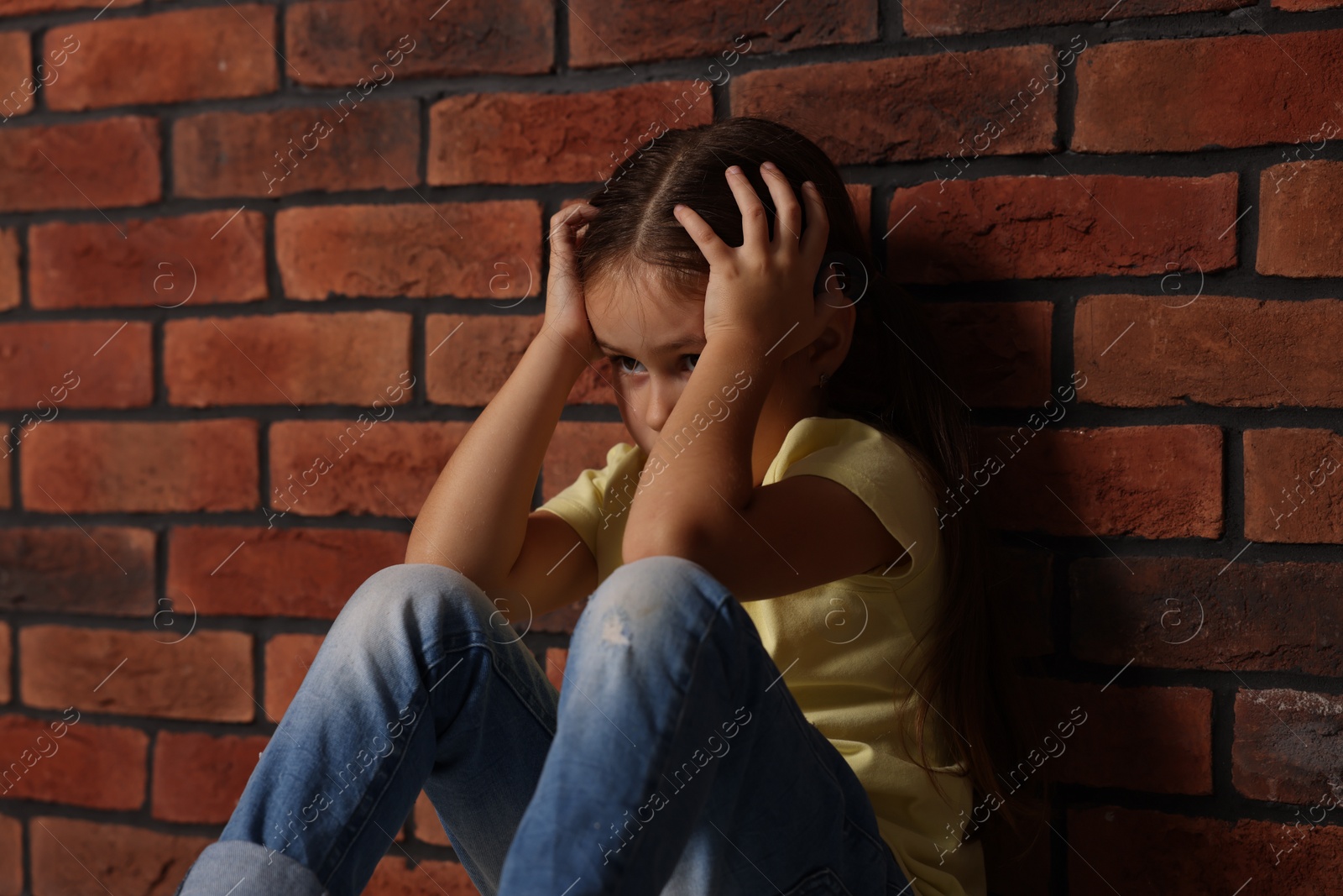 Photo of Child abuse. Upset little girl near brick wall