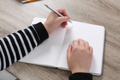 Photo of Woman writing in notebook at wooden table, closeup