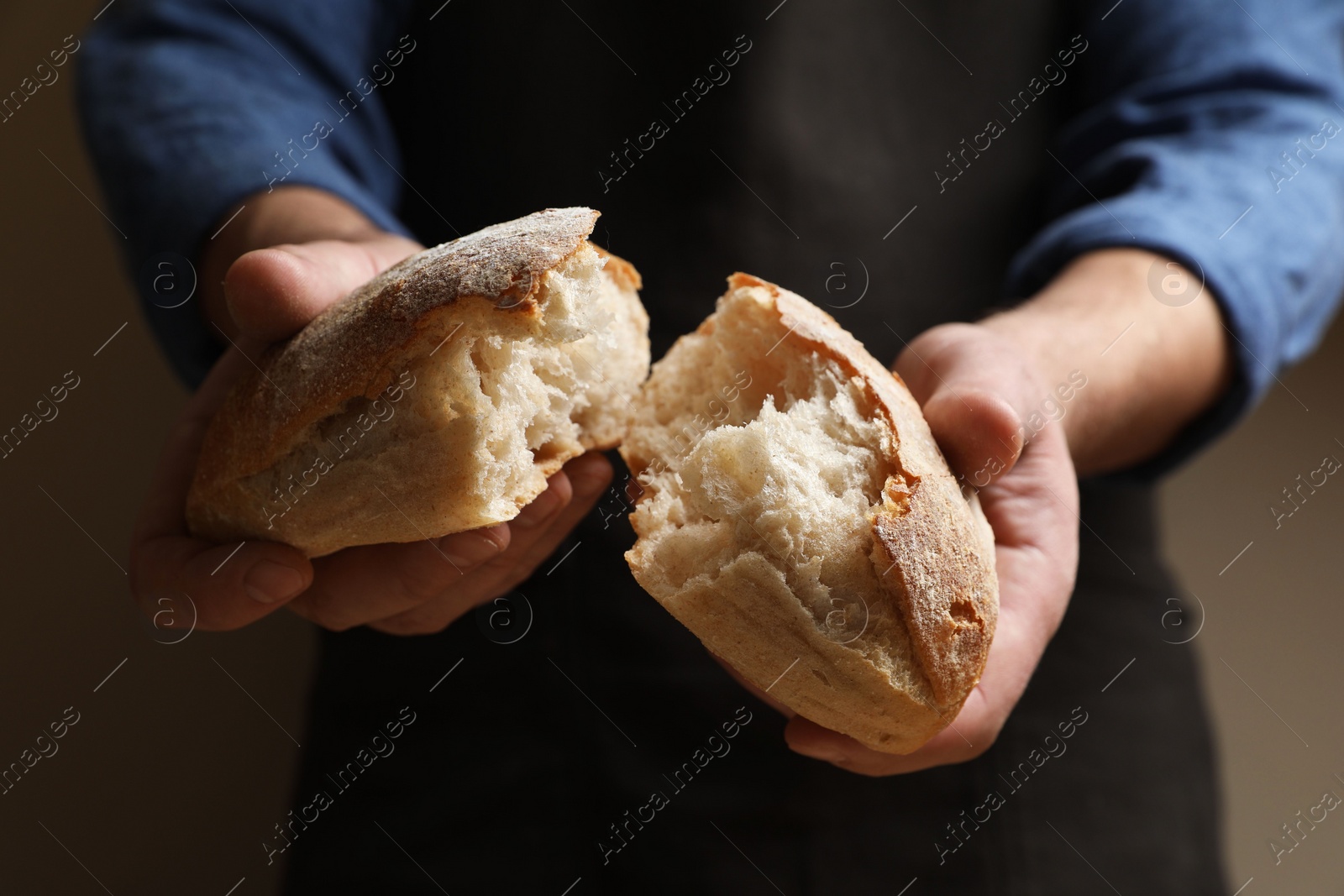 Photo of Man breaking loaf of fresh bread on dark background, closeup