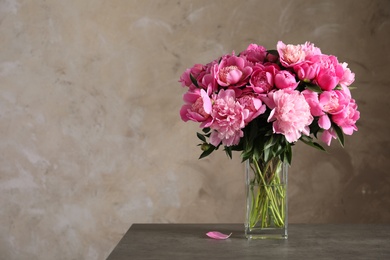 Photo of Fragrant peonies in vase on table against color background, space for text. Beautiful spring flowers