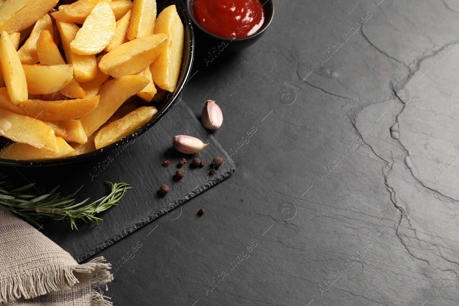 Photo of Plate with tasty baked potato wedges, rosemary, garlic and sauce on black table, above view. Space for text