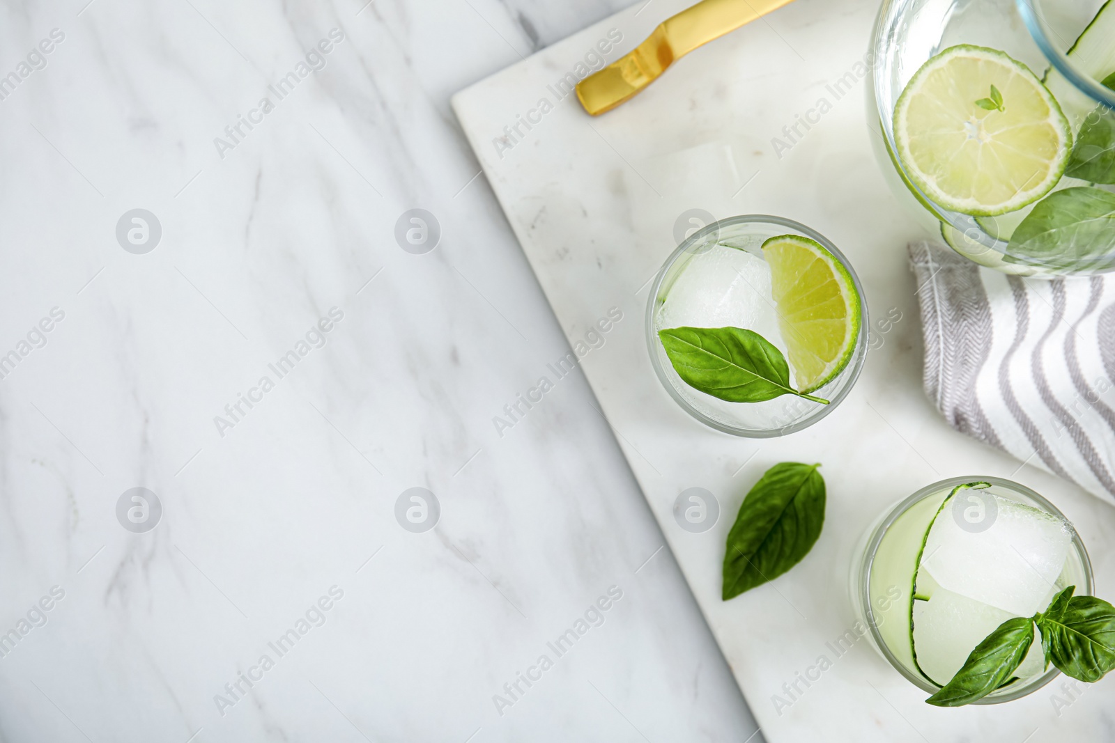 Photo of Tasty fresh cucumber water with sliced lime and basil on white marble table, flat lay. Space for text
