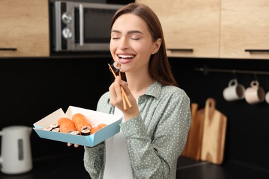 Beautiful young woman eating sushi rolls with chopsticks in kitchen