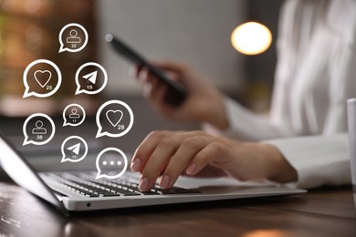 Different virtual icons and young woman using laptop and smartphone at table indoors, closeup. SMM (Social media marketing) concept