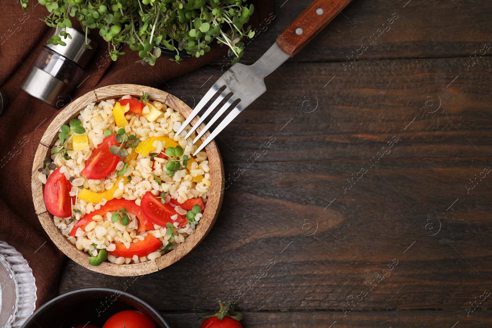 Photo of Cooked bulgur with vegetables in bowl on wooden table, flat lay. Space for text