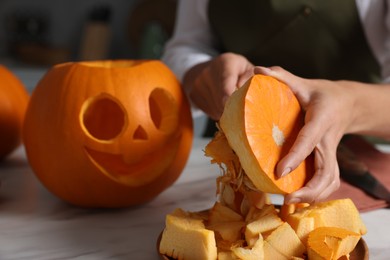 Woman carving pumpkin for Halloween at white marble table, closeup